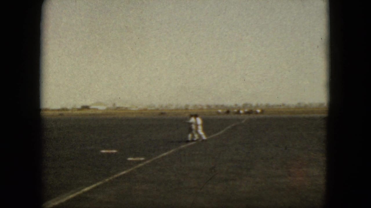 Ground crew member walks across a wide runway with aircraft in the distance.
