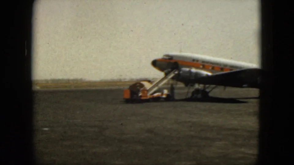 Commercial airliner with mobile boarding stairs is parked on the Acapulco airport tarmac in 1962 home-movie footage.