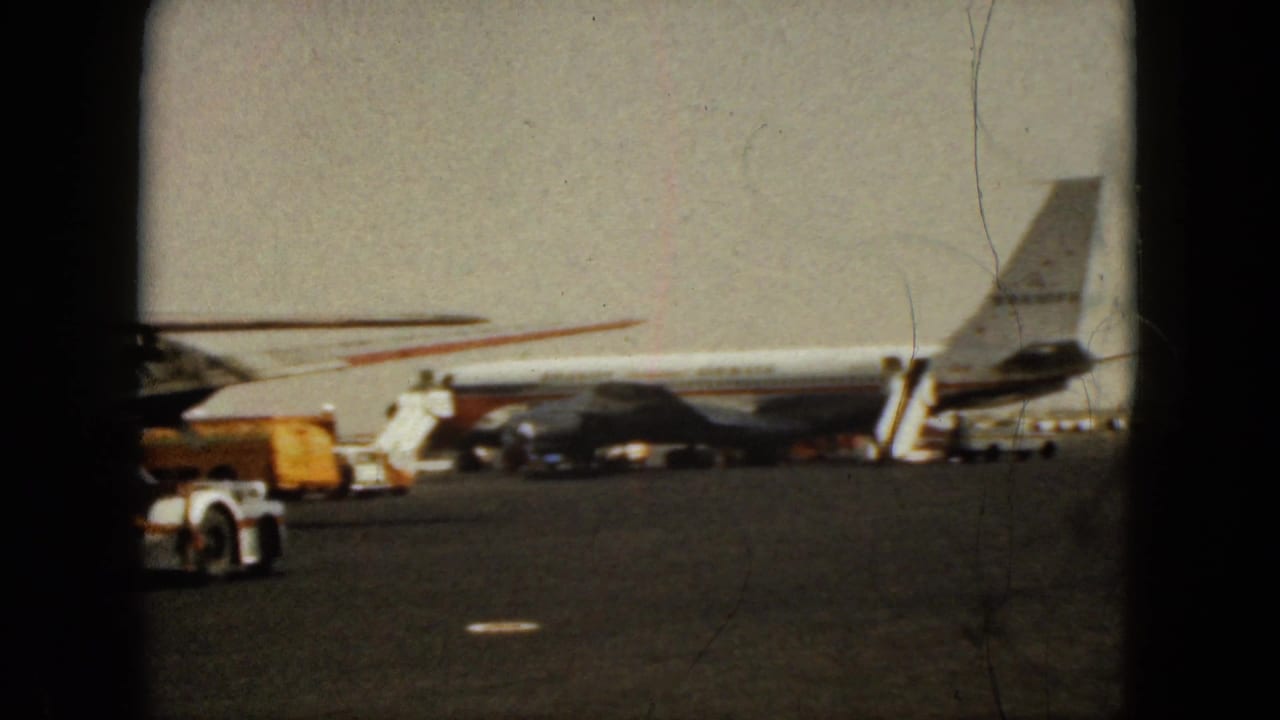 Jet airliner beside mobile stairs and service equipment on a sunlit airport apron.