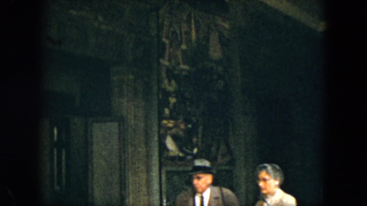 Two adult visitors sit or stand near a dark carved interior wall.