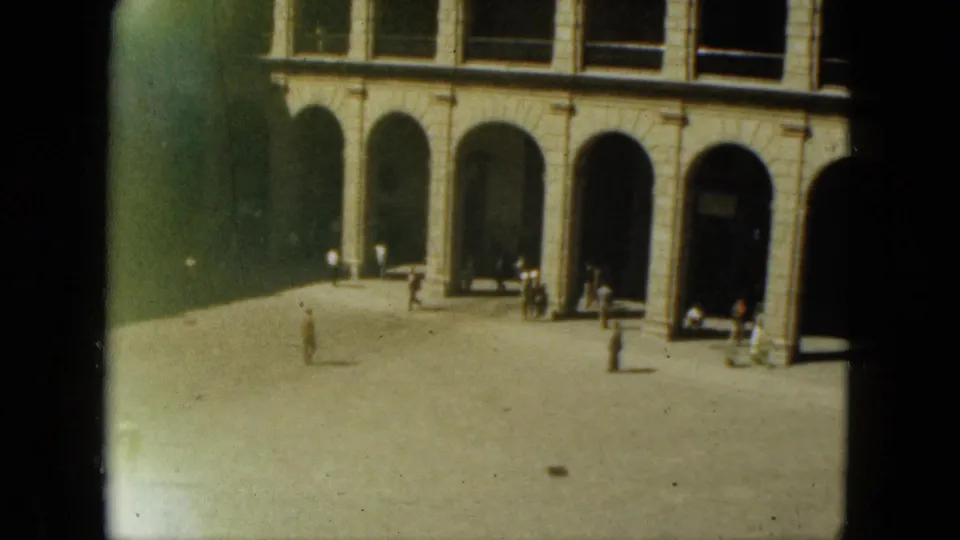 1962 Acapulco home-movie frame showing a bright stone plaza, arched colonnades, deep shade, and scattered pedestrians.