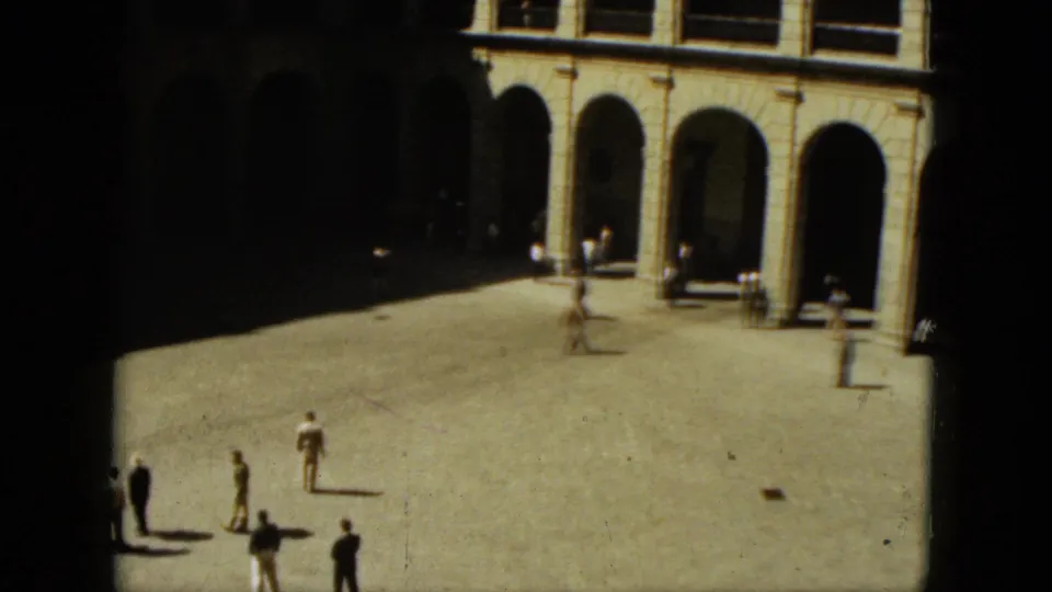 Wide 8mm view of a sunlit Acapulco plaza with several people crossing near shaded arched colonnades.