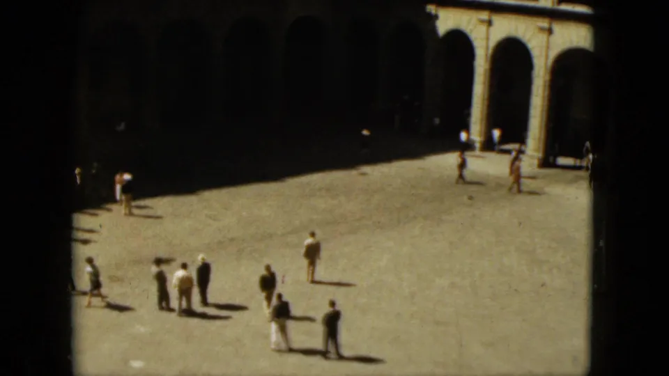 1962 Acapulco frame with people pausing and walking across a sunlit plaza beneath a shaded arched arcade.
