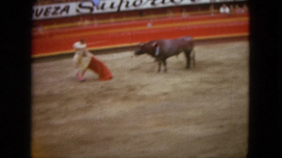 A matador in light costume pulls the red cape while the dark bull turns on the dirt floor of the 1962 Acapulco bullring.