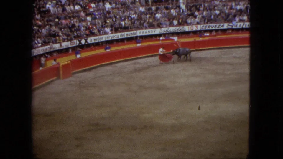 1962 Acapulco home-movie frame showing a matador with red cape facing a dark bull in a large arena with spectators.
