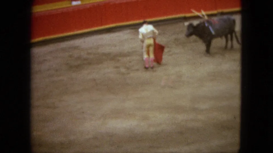1962 Acapulco bullring frame with a matador holding a lowered red cape as the bull pauses several steps away.