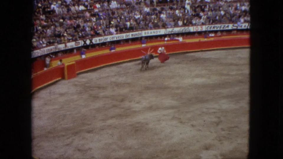1962 Acapulco bullfight scene with a matador using a red cape as the bull moves near the red ring barrier and crowd.