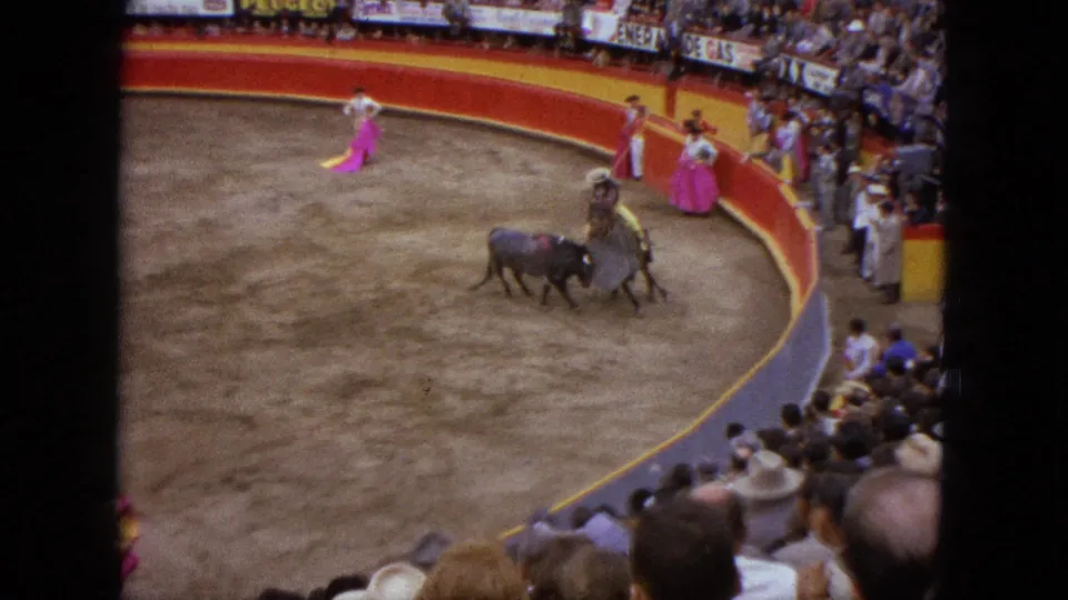 1962 Acapulco home-movie view of a bull and matador in a ring, with other cape holders and a packed crowd around the arena.