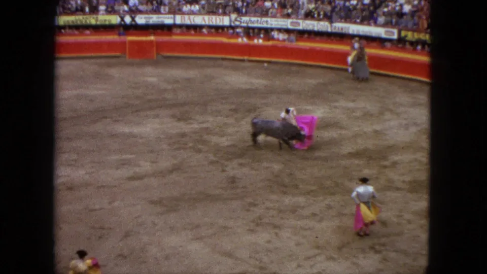 1962 Acapulco bullring view with a matador using a pink cape near a black bull as spectators watch from the stands.