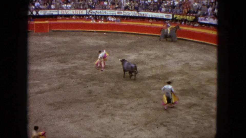 Visitor-shot 1962 Acapulco bullfight frame with a black bull in the ring, matadors with colored capes, and packed spectator seating.