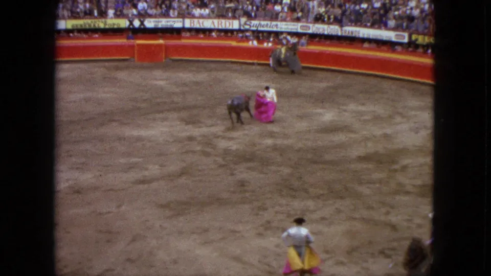 In a 1962 Acapulco bullring, a matador holds a pink cape near a dark bull as spectators fill the stands.