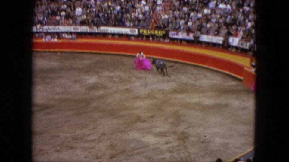 Spectator view in Acapulco, 1962, with a bull moving toward a matador's pink cape inside the crowded arena.