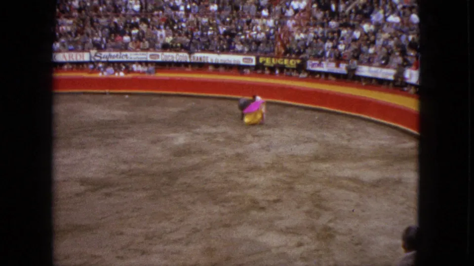 The matador turns with the pink and yellow cape after the bull passes, seen from a distant home-movie angle in Acapulco.