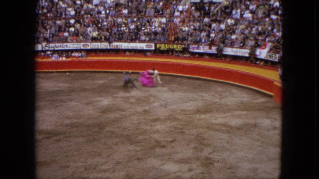 1962 Acapulco bullring scene with a matador in white handling a pink cape as a dark bull approaches before packed stands.