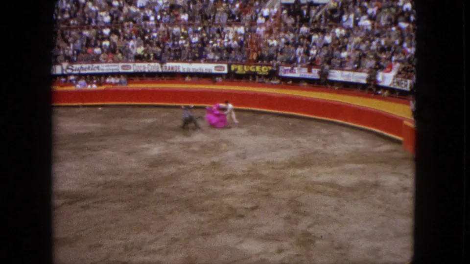 1962 Acapulco bullring scene with a matador in white handling a pink cape as a dark bull approaches before packed stands.