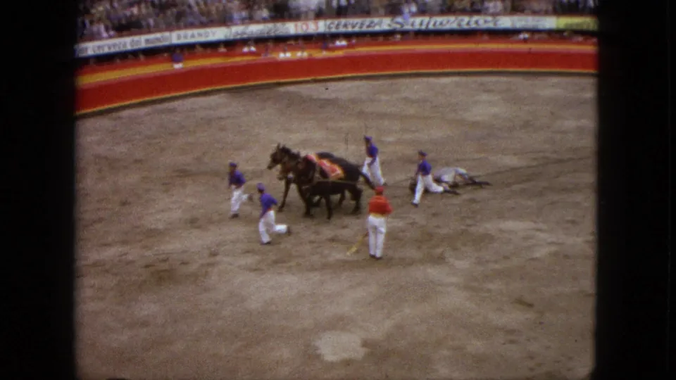 1962 Acapulco bullring view with attendants, a horse-drawn team, and a fallen figure on the sand before a packed crowd.