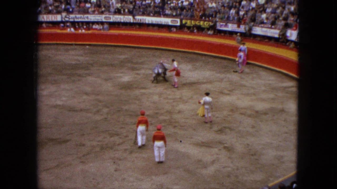 High-angle 1962 Acapulco bullring view shows the bull moving past a matador while other figures wait near the barrier and ring floor.