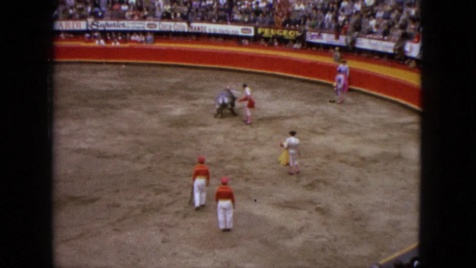 High-angle 1962 Acapulco bullring view shows the bull moving past a matador while other figures wait near the barrier and ring floor.