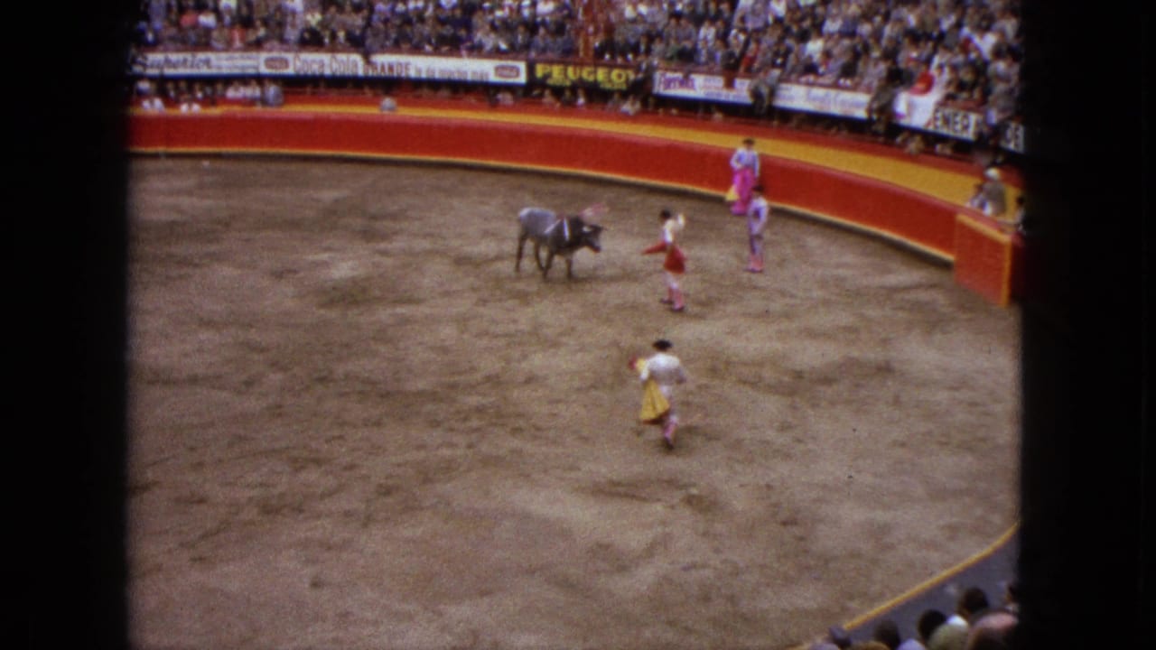 1962 Acapulco bullfighting scene from an elevated spectator view, with a bull, matadors in colorful outfits, red barriers, and crowded stands.