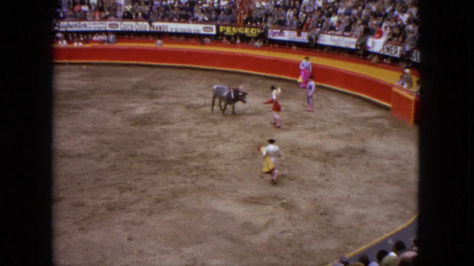 1962 Acapulco bullfighting scene from an elevated spectator view, with a bull, matadors in colorful outfits, red barriers, and crowded stands.