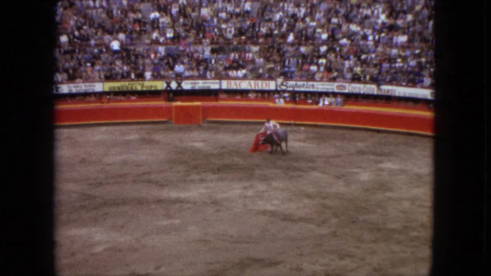 1962 Acapulco bullfight scene with a matador holding a red cape before a bull in a sandy arena.