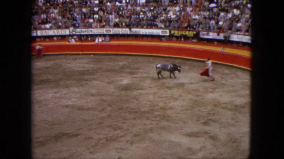 Acapulco bullfight frame showing a matador extending a red cape toward a bull in the ring.