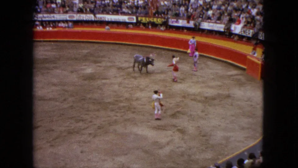 Wide 1962 Acapulco arena view with a bull, matador, assistants, crowd, and visible advertising around the ring.