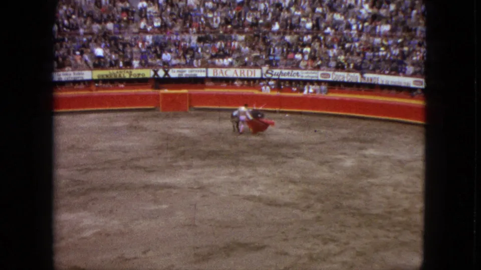 1962 Acapulco arena view shows a matador holding a red cape near a grey bull, with spectators and sponsor signs behind the ring.
