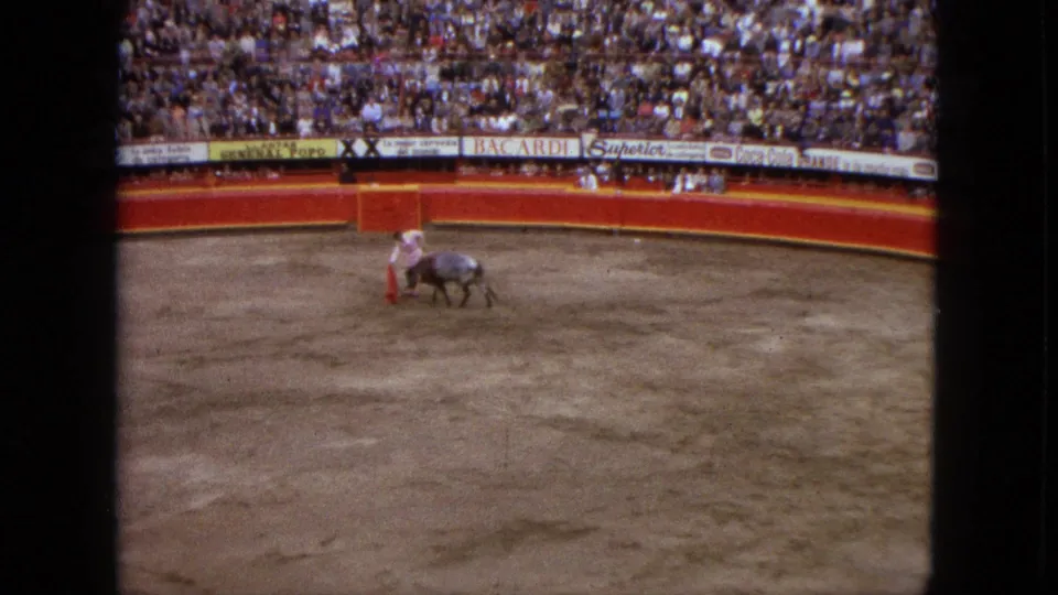 Distant 8mm view from Acapulco in 1962 showing the matador and bull passing near each other on the dirt arena floor.