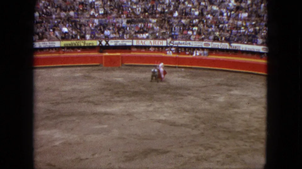 Wide Acapulco bullring frame from 1962 with the matador and bull separated on the arena floor below crowded stands.