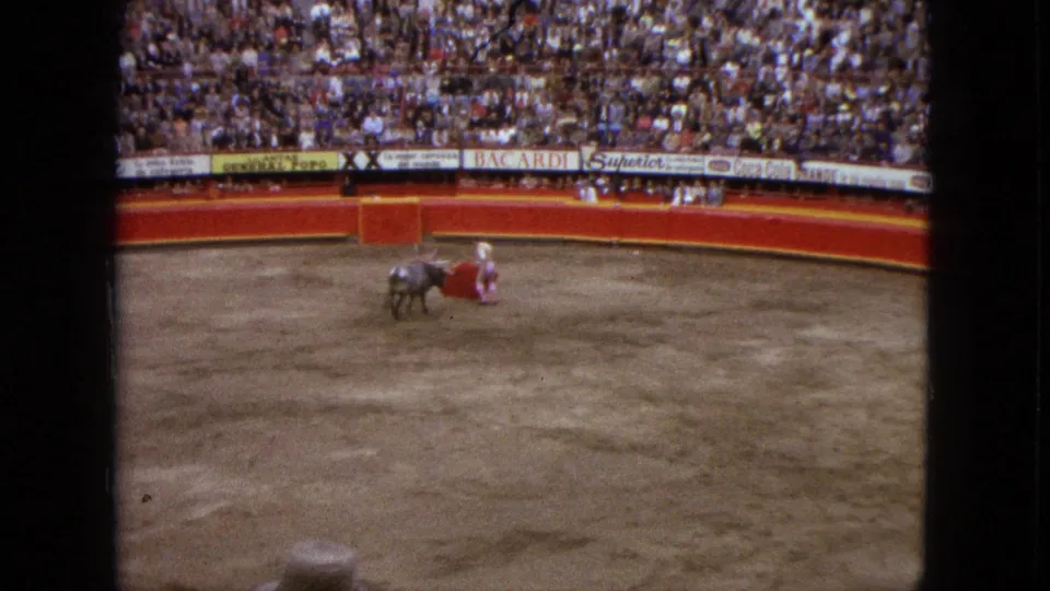 A matador in pink and white stands close to the bull while extending a red cape across the dusty Acapulco bullring.