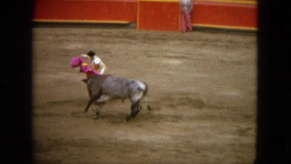 In 1962 Acapulco footage, a matador presents a purple cape as a bull moves across the sandy arena.