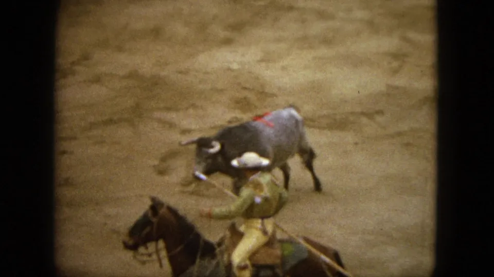 1962 Acapulco 8mm frame showing a rider on a dark horse near a grey bull in a dusty arena.