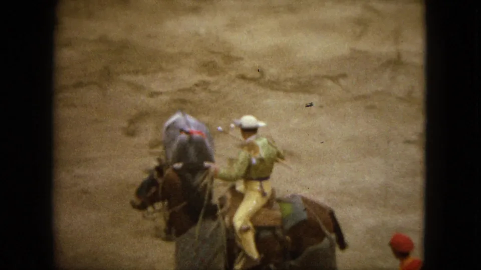 1962 Acapulco home-movie frame with a grey bull between mounted riders and a visible spectator near the lower edge.