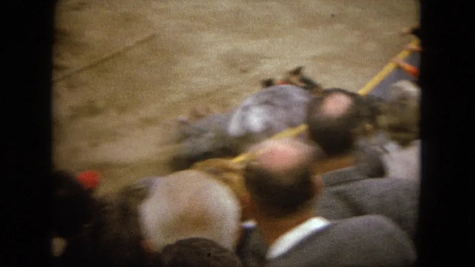 1962 Acapulco home-movie frame from the stands, with spectators in front and a grey bull and riders in the arena beyond.