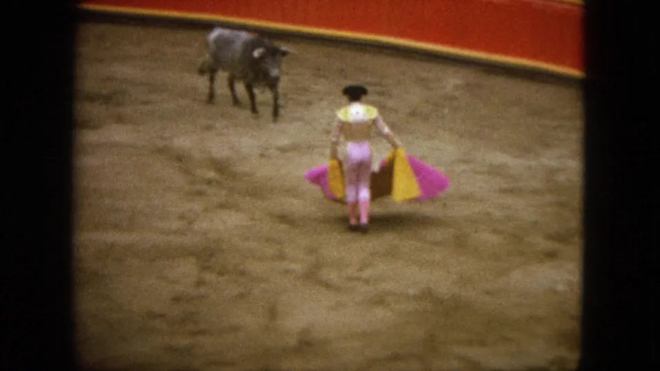 1962 Acapulco home-movie frame of a matador standing in the sand ring with a bull nearby and cape spread.