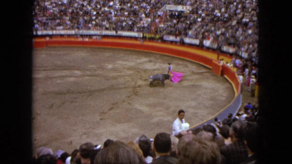 1962 Acapulco home-movie view of a matador working a pink cape near a bull as spectators fill the arena.