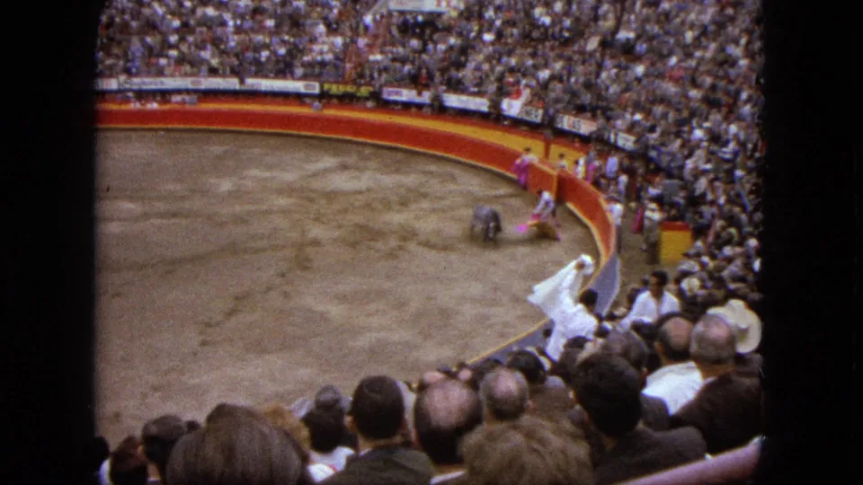 Spectator-shot 8mm frame from Acapulco showing bullfight action near the barrier with crowd and cape movement.