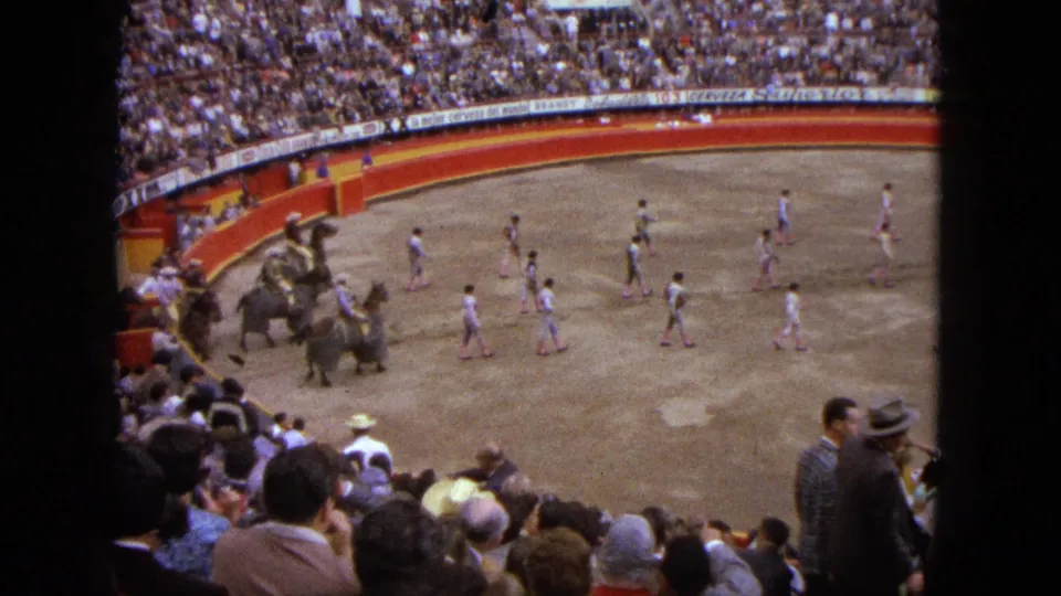 Spectator-shot 8mm frame from Acapulco showing camels, riders, walkers, and a dense bullring crowd.
