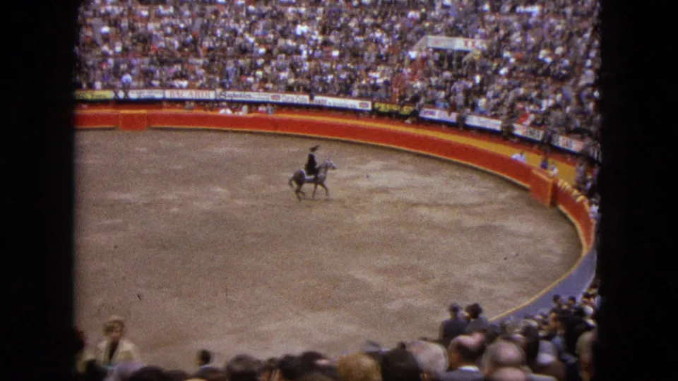 1962 Acapulco frame with a mounted rider near the red and yellow arena barrier and packed spectator seating.