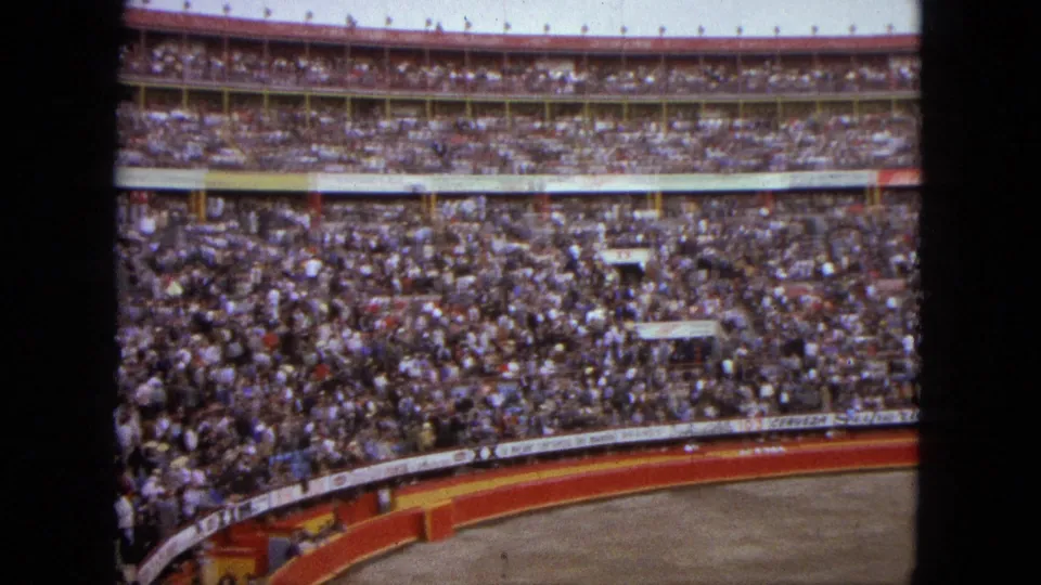 Acapulco 1962 frame showing spectators packed into tiered stands above the curved red and yellow edge of an arena.