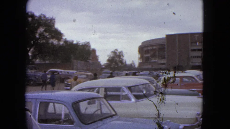 1962 Acapulco frame with pastel mid-century cars, small pedestrian figures, trees, and the edge of a TOREO arena building.
