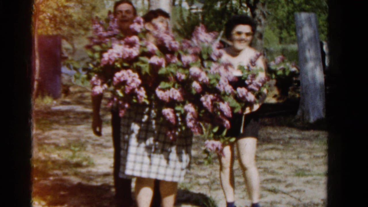 Three adults stand in a garden holding large purple lilac bouquets.