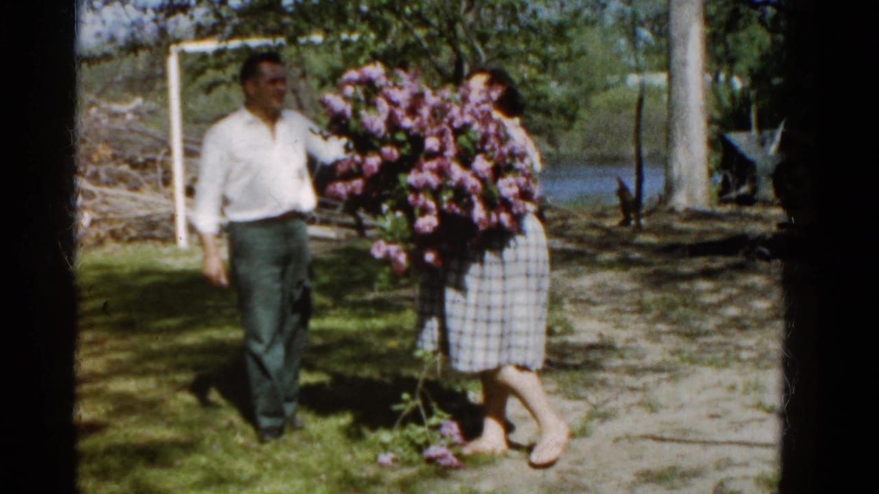 Woman in plaid dress holding a large lilac bouquet beside a man in a yard.