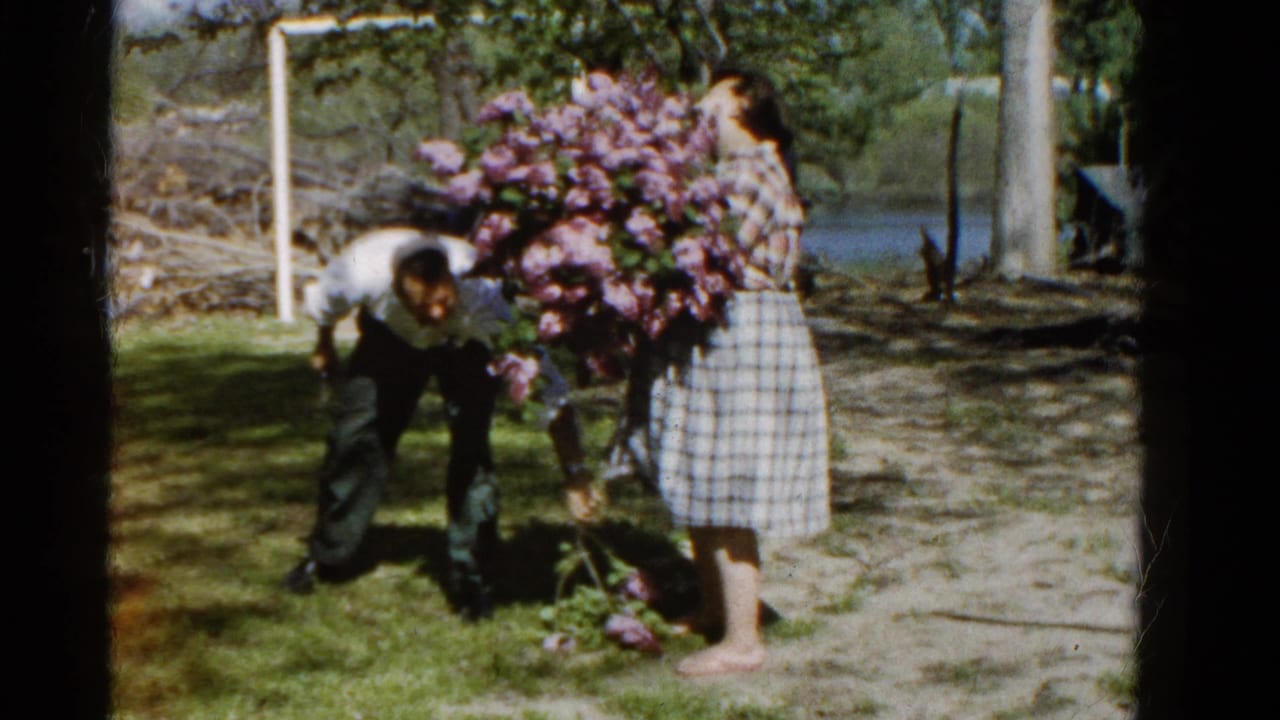 In the Wauconda yard scene, the man bends down to gather fallen lilacs as the woman steadies the bouquet.