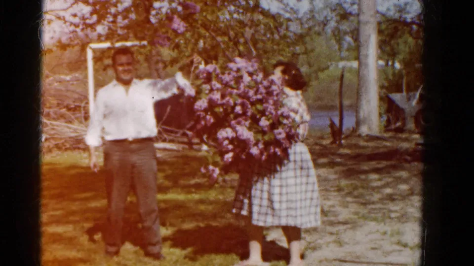 A warm, slightly faded 1961 Wauconda 8mm frame shows the man standing by as the woman holds the lilac bouquet.