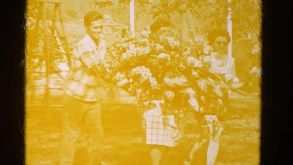 Yellow exposure dominates the final 8mm frame as the man and woman remain near the large lilac bouquet in the Wauconda yard.