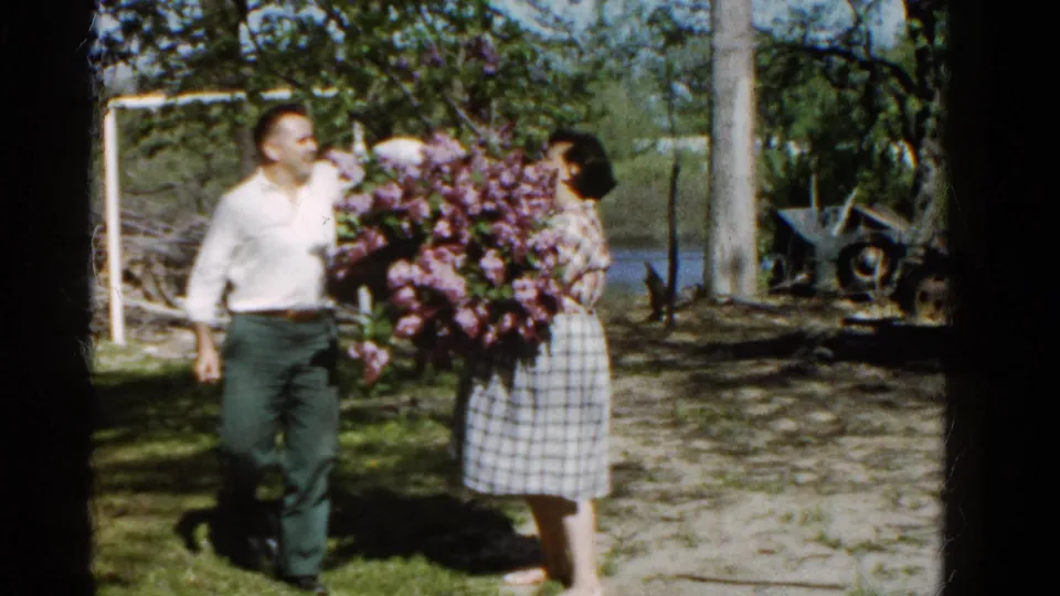 The man and woman face each other beside the purple lilac bouquet in 1961 home-movie footage from Wauconda.