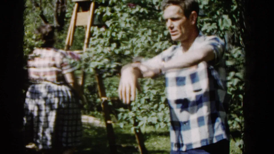 Late frame from the 1961 Wauconda garden clip with the man gesturing in profile while the woman moves away near plants and a wooden ladder.
