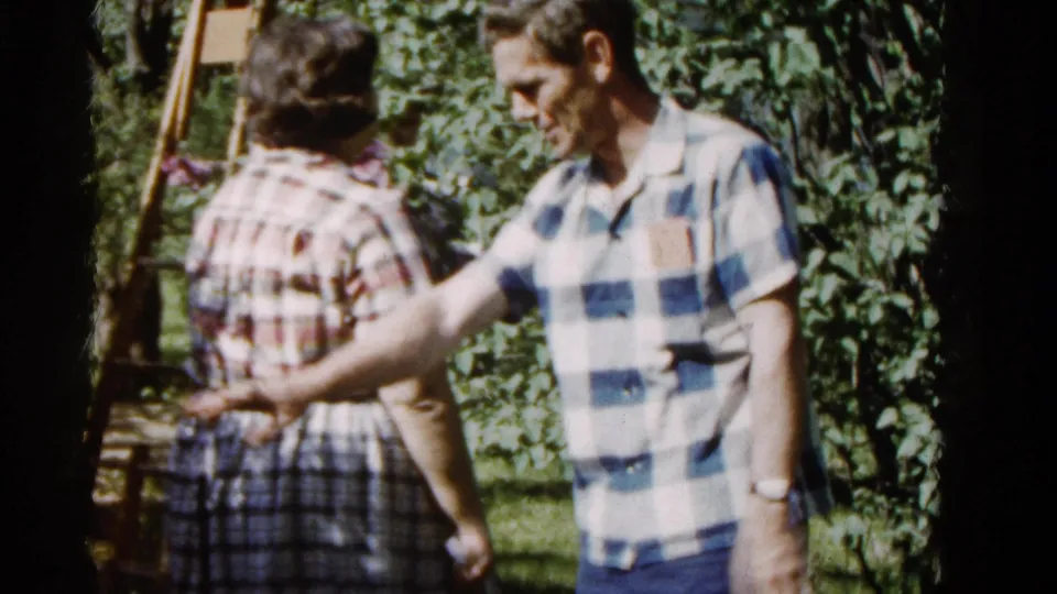 The man gestures toward the woman near blooming lilacs in this 1961 Wauconda home-garden moment.